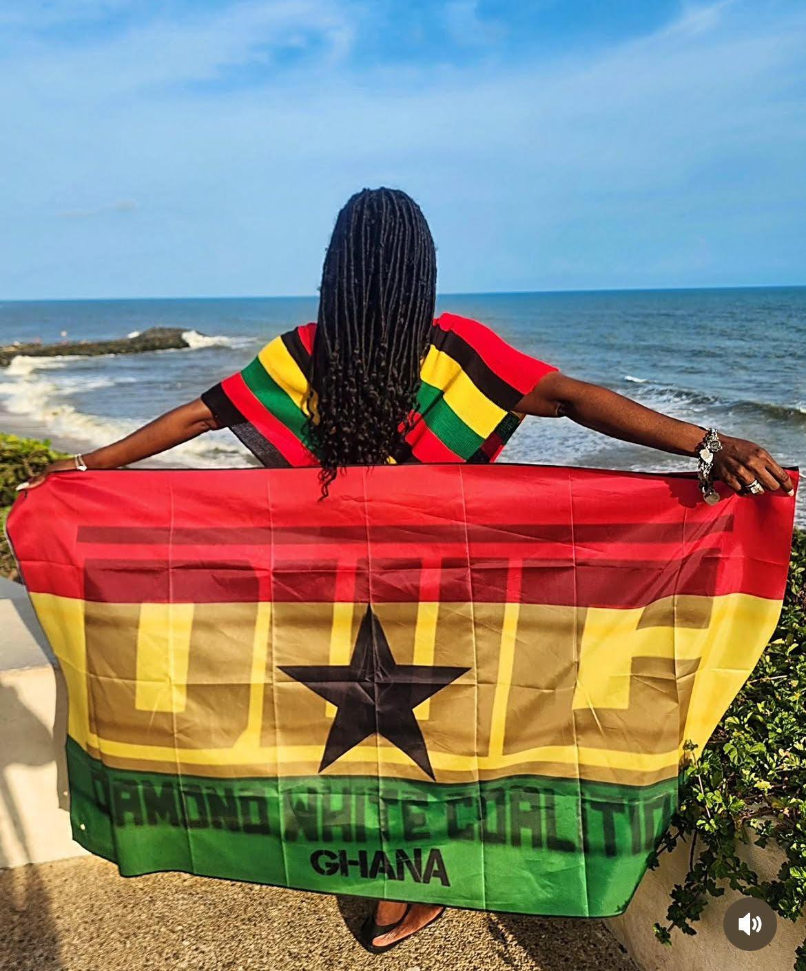 Diamond White holding the Ghana flag beside the ocean